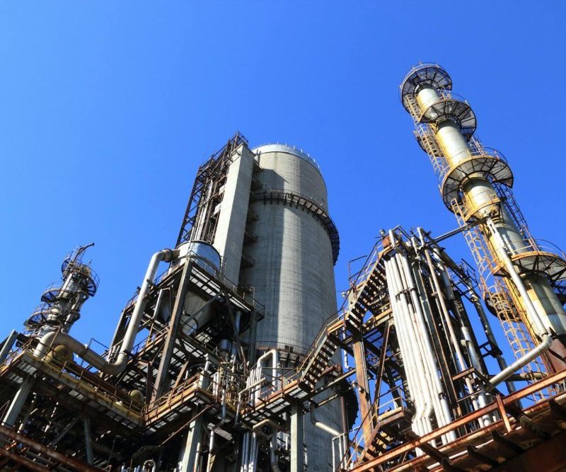 A towering industrial plant under a vivid blue sky, showcasing its intricate architecture and industrial prowess.