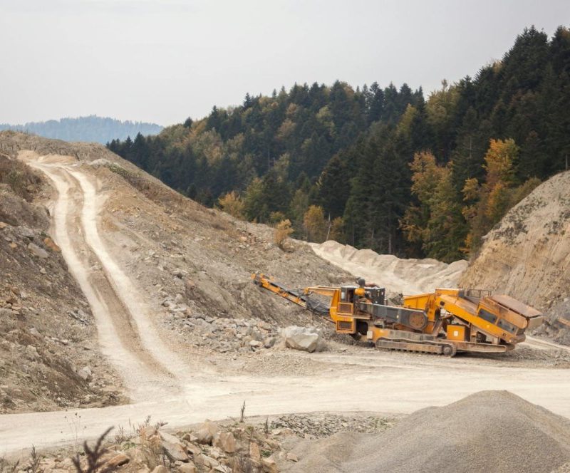 Industrial machinery operating in a forest quarry landscape during daytime.