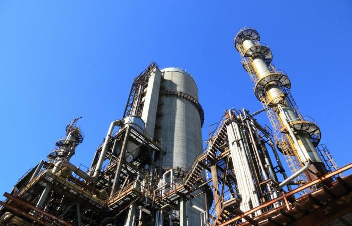 A towering industrial plant under a vivid blue sky, showcasing its intricate architecture and industrial prowess.