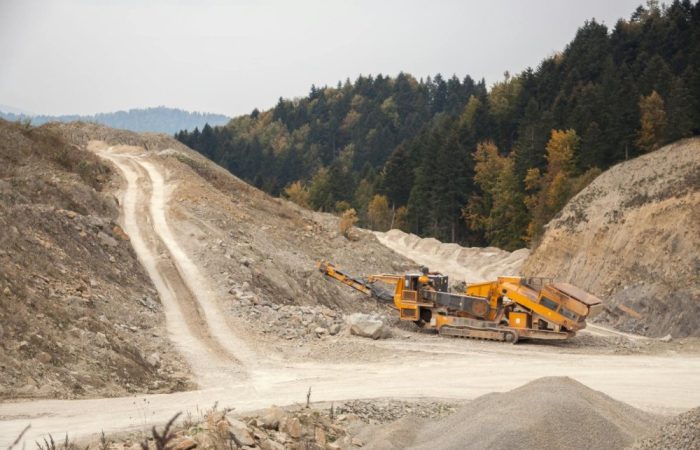 Industrial machinery operating in a forest quarry landscape during daytime.